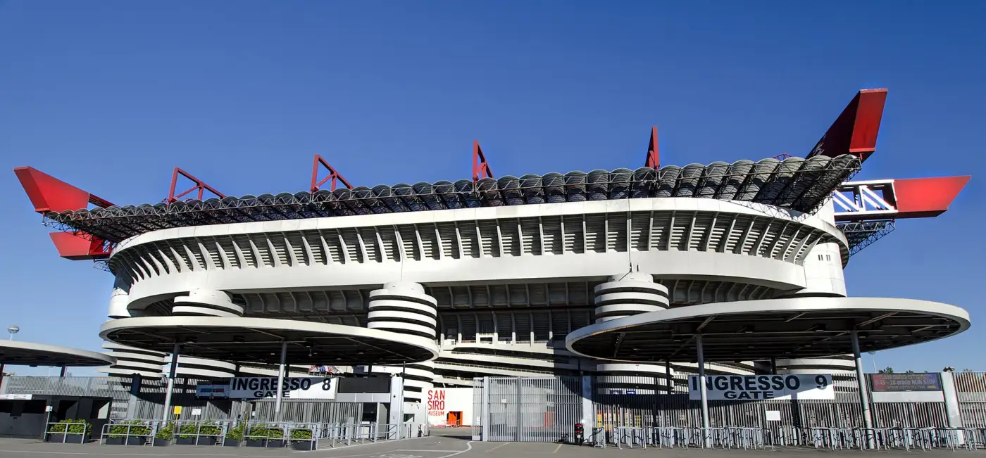 Le stade Giuseppe-Meazza de San Siro à Milan, tours cylindriques à rampes, anneaux de béton et poutres rouges du toit sous un ciel bleu