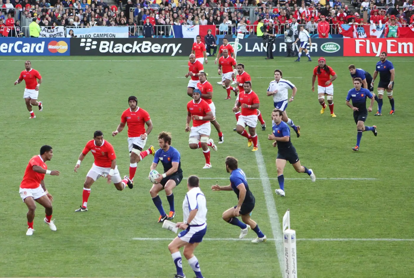 Match de rugby France-Tonga en 2011 au stade de Wellington, un joueur français en maillot bleu porte le ballon face à plusieurs joueurs tongiens en rouge