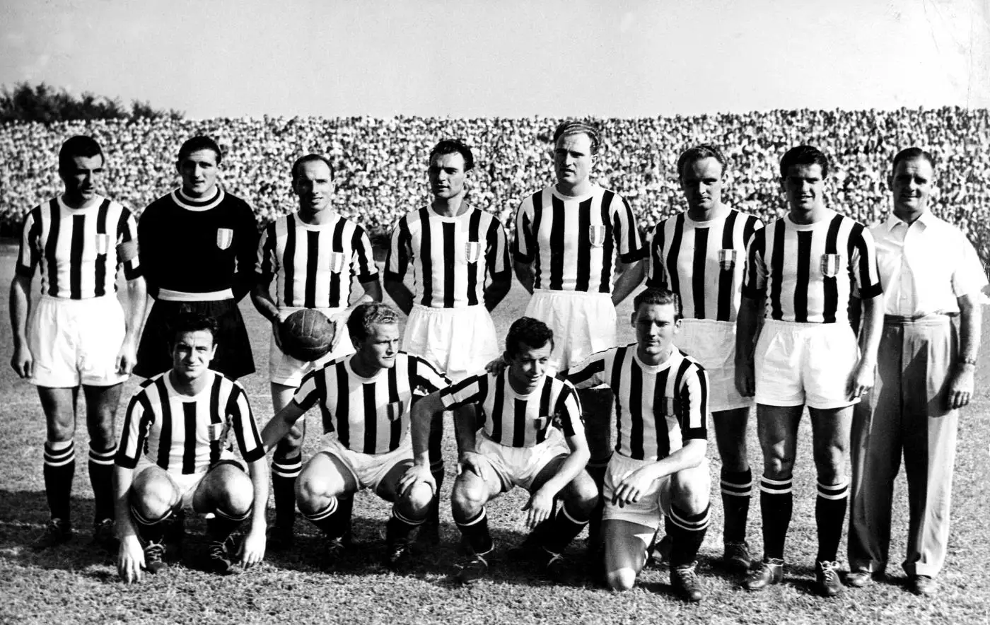 Photo en noir et blanc de l'équipe de la Juventus posant avant un match en 1950, onze joueurs en maillots rayés portant l'écusson tricolore et leur entraîneur, devant une tribune noire de monde