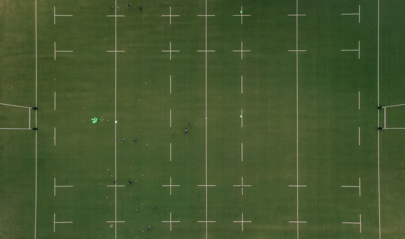 Terrain de rugby vu du ciel à Agen, avec ses lignes blanches, ses poteaux et quelques joueurs à l'entraînement