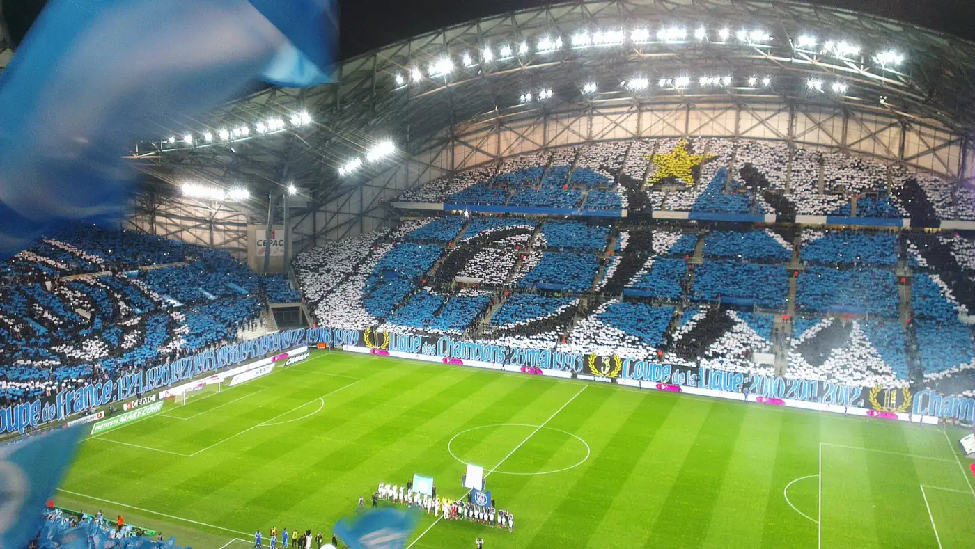 Tribunes du Stade Vélodrome couvertes d'un tifo bleu et blanc aux couleurs de l'Olympique de Marseille, joueurs alignés sur la pelouse avant le coup d'envoi