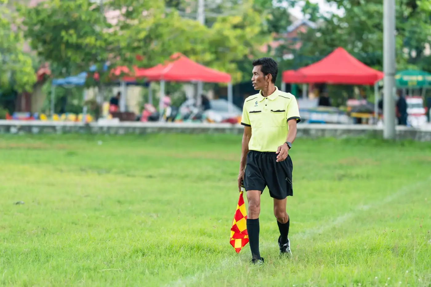 Un arbitre assistant en maillot jaune tient son drapeau à damier le long d'un terrain de football en herbe