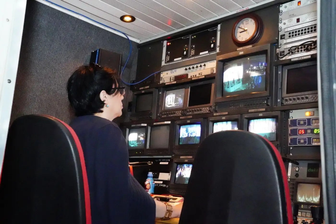 Une régie de télévision avec un mur d'écrans de contrôle et une opératrice de dos devant le pupitre