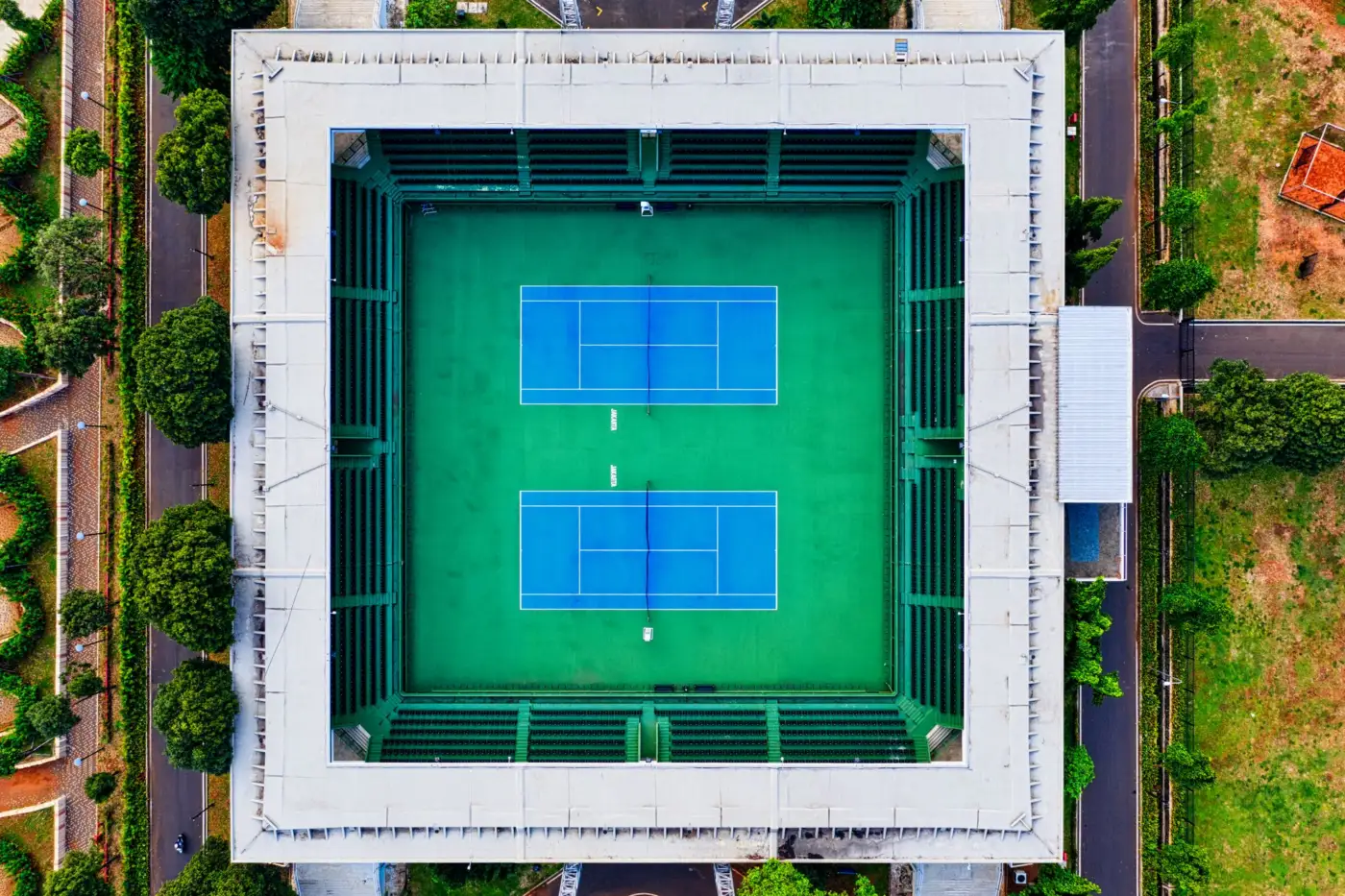 Stade de tennis vu du ciel, deux courts bleus au centre d'une arène aux tribunes vertes
