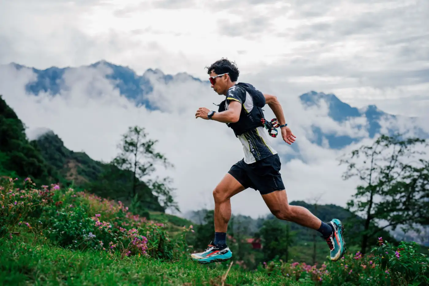 Un coureur de trail en pleine foulée sur un sentier de montagne, au-dessus d'une mer de nuages