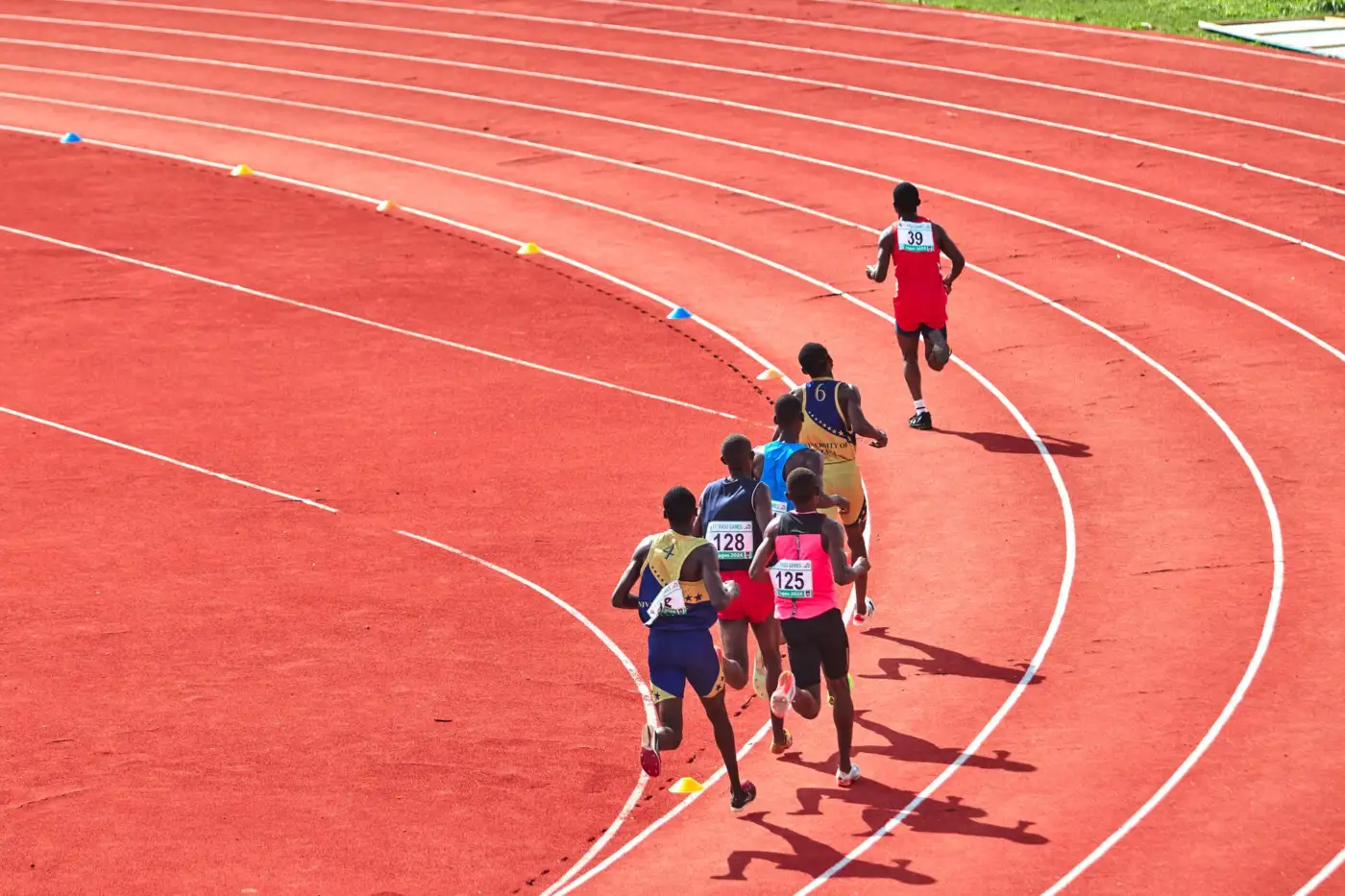 Un groupe de coureurs en file sur la courbe d'une piste d'athlétisme rouge, vus de dos et d'en haut