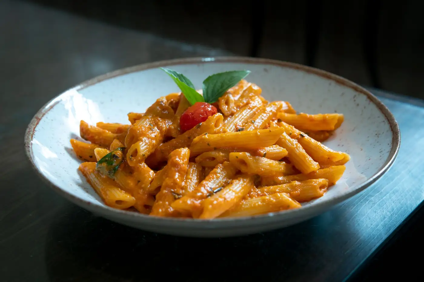 Une assiette creuse de penne à la sauce tomate garnie de basilic, posée sur une table sombre